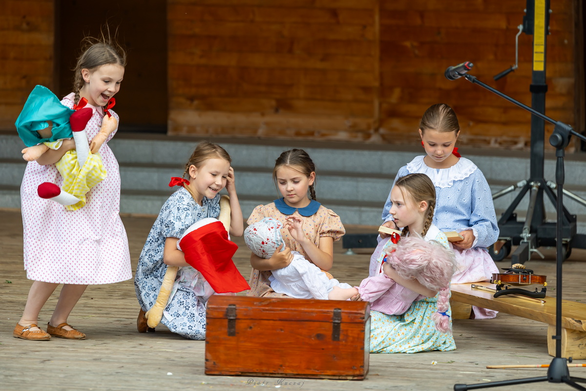 Występ zespołu: dziewczynki bawią się lalkami przy drewnianej skrzyni.