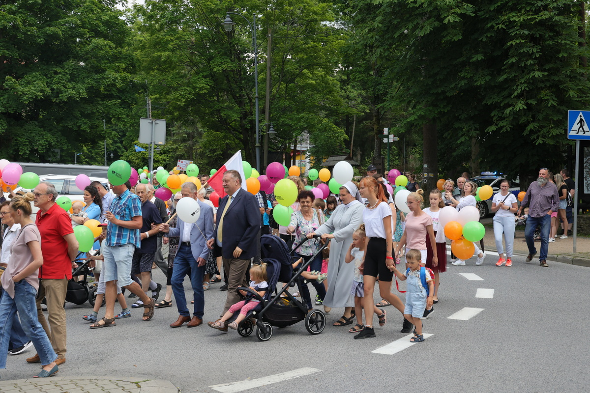 Pochód ludzi idący ulicą. Uczestnicy niuosą kolorowe baloniki.