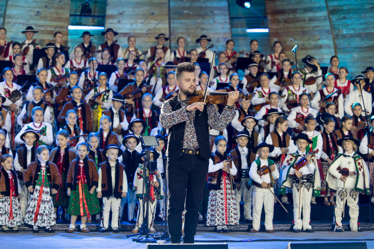 Damian Pałasz grający na skrzypcach przed chórem górali.