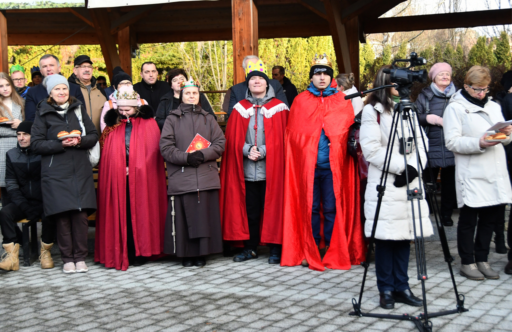 Trzej uczestnicy orszaku przebrani w czerwone peleryny i ze złotymi koronami na głowach pomiędzy pozostałymi ludźmi.